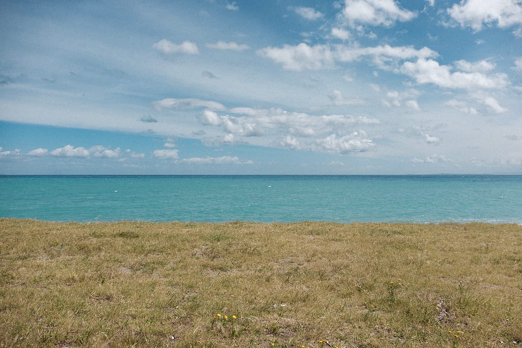 Prato, mare turchese e cielo con nuvole, in tre fasce orizzontali