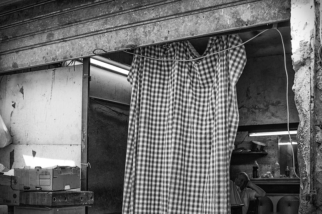 Tenda a quadretti davanti a una bottega, un uomo riposa all'interno