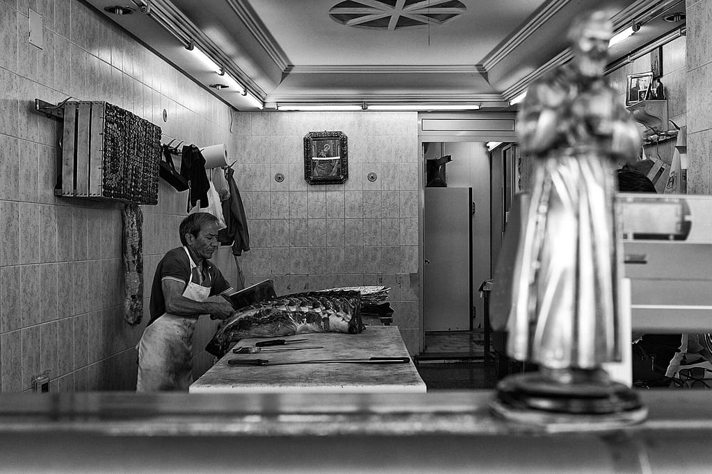 Macellaio al lavoro in una bottega di Palermo, una statua di santo in primo piano