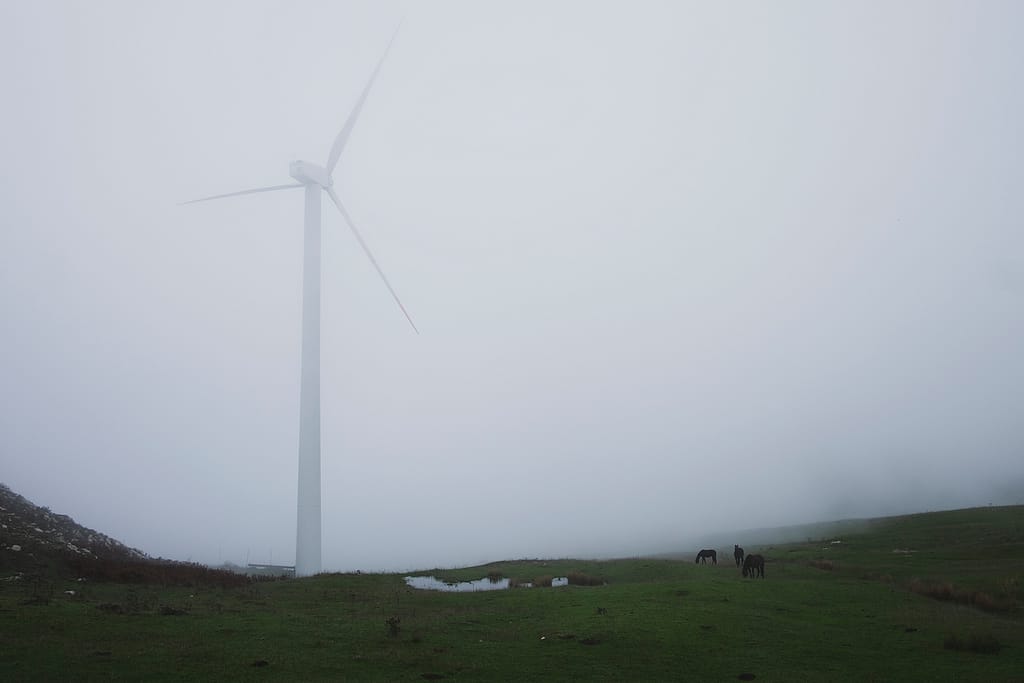 Una pala eolica che sparisce nella nebbia sopra un prato di montagna