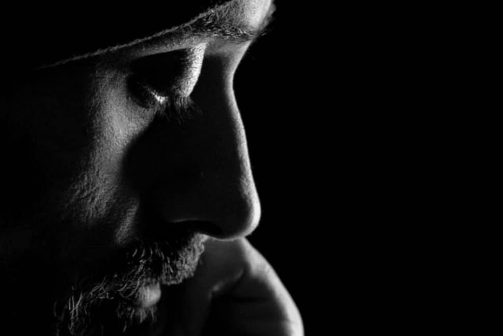 Ritratto in bianco e nero di un uomo con la barba, di profilo, su fondo nero.