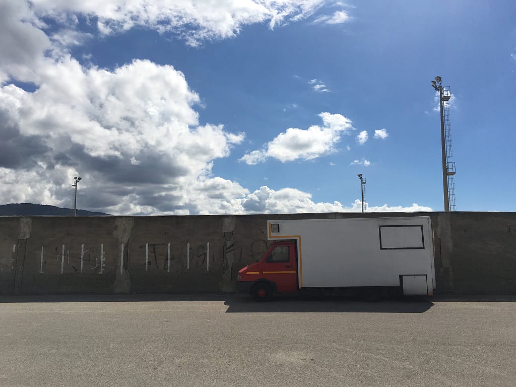 Furgone rosso e bianco parcheggiato davanti a un muro di cemento sotto un cielo con nuvole, Torrenova