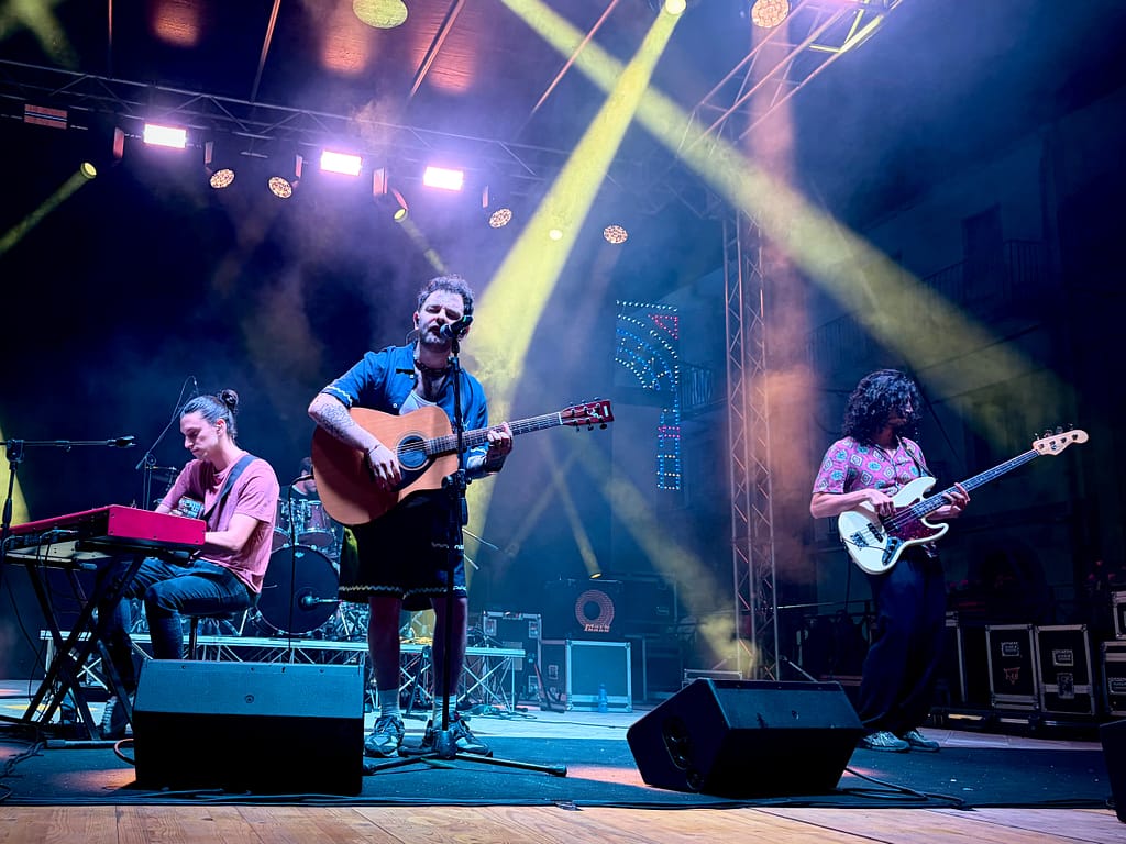 Fotografare un concerto con lo smartphone: band sul palco in piazza a Floresta, con fasci di luce e luminarie