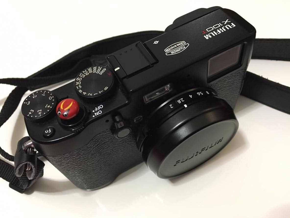 Fujifilm X100T nera con il tappo dell’obiettivo e un pulsante di scatto rosso