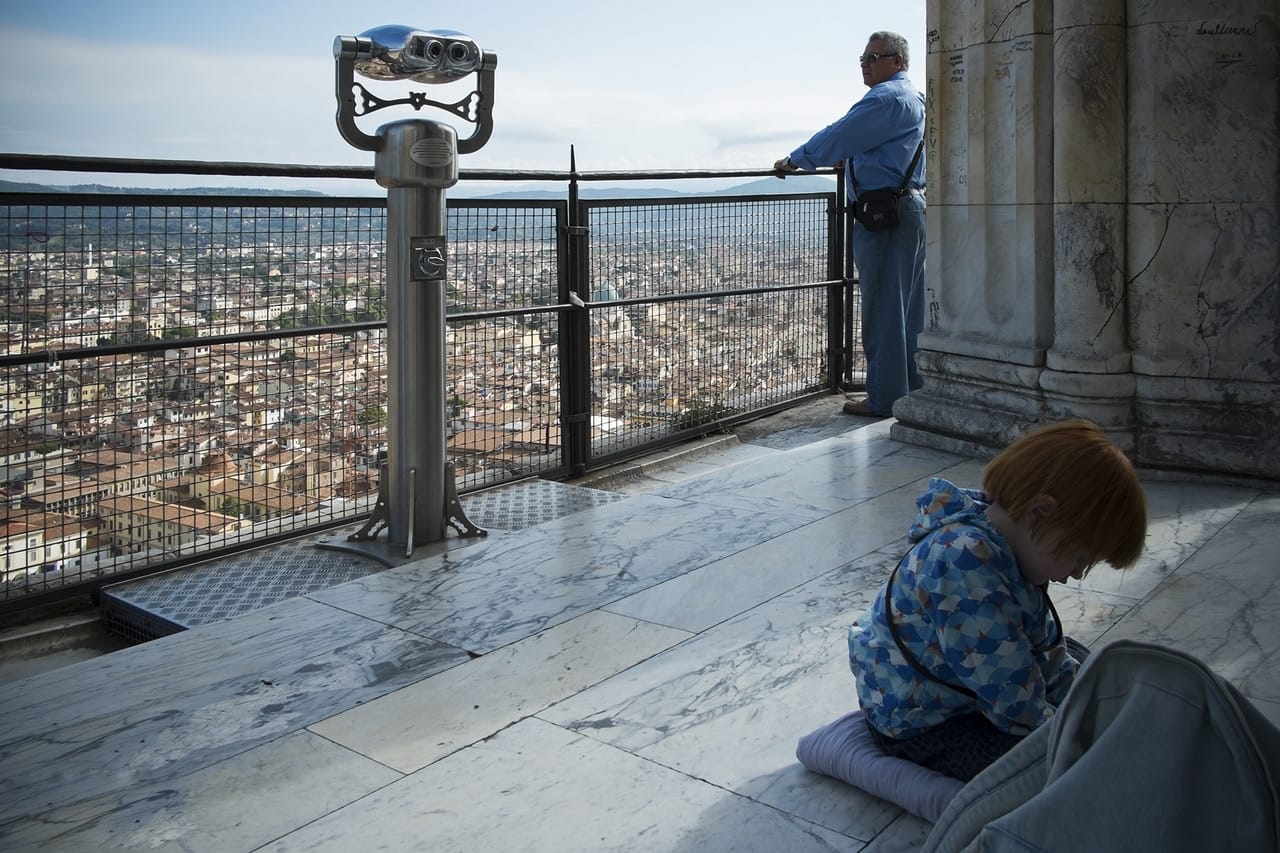 Terrazza in cima alla cupola di Firenze con un cannocchiale panoramico, un uomo che guarda la città e un bambino seduto a terra