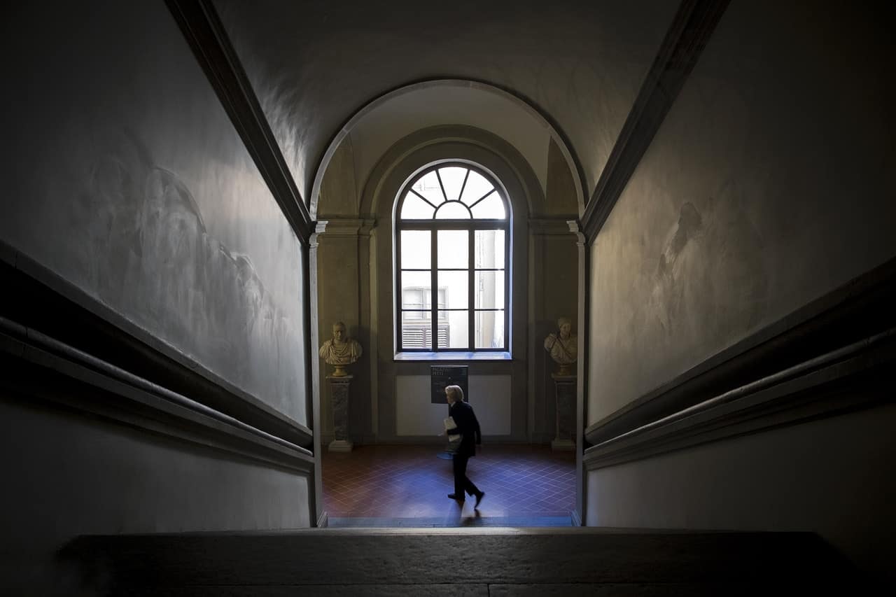 Lo scalone di Palazzo Pitti a Firenze, con una finestra ad arco in fondo e una persona che passa nella luce