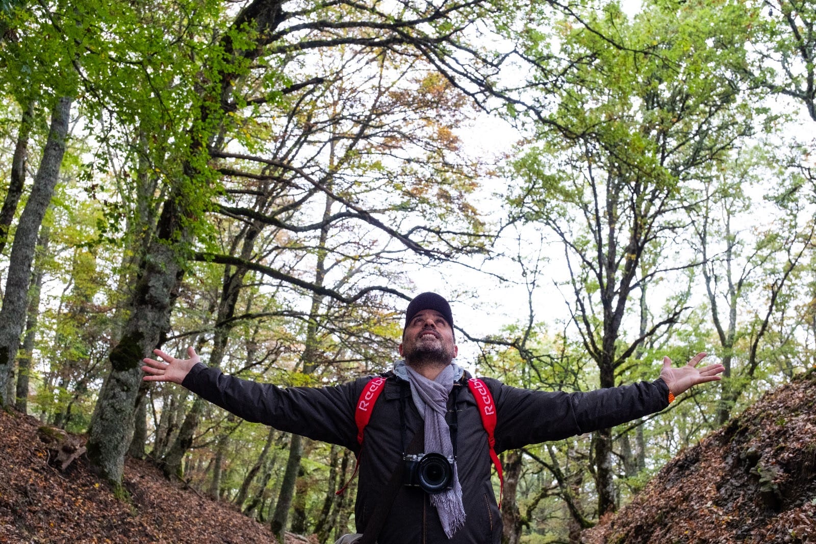 Daniele Tranchita a braccia aperte in un bosco, con la fotocamera al collo