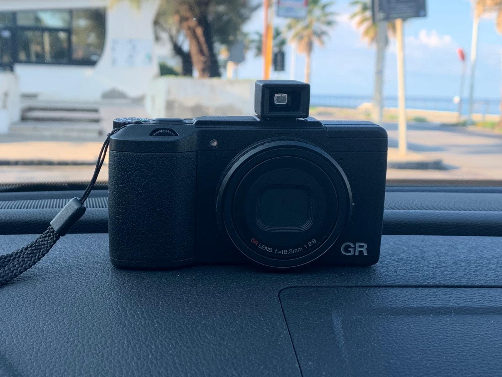La Ricoh GR II con il mirino esterno, appoggiata sul cruscotto di un’auto davanti al lungomare