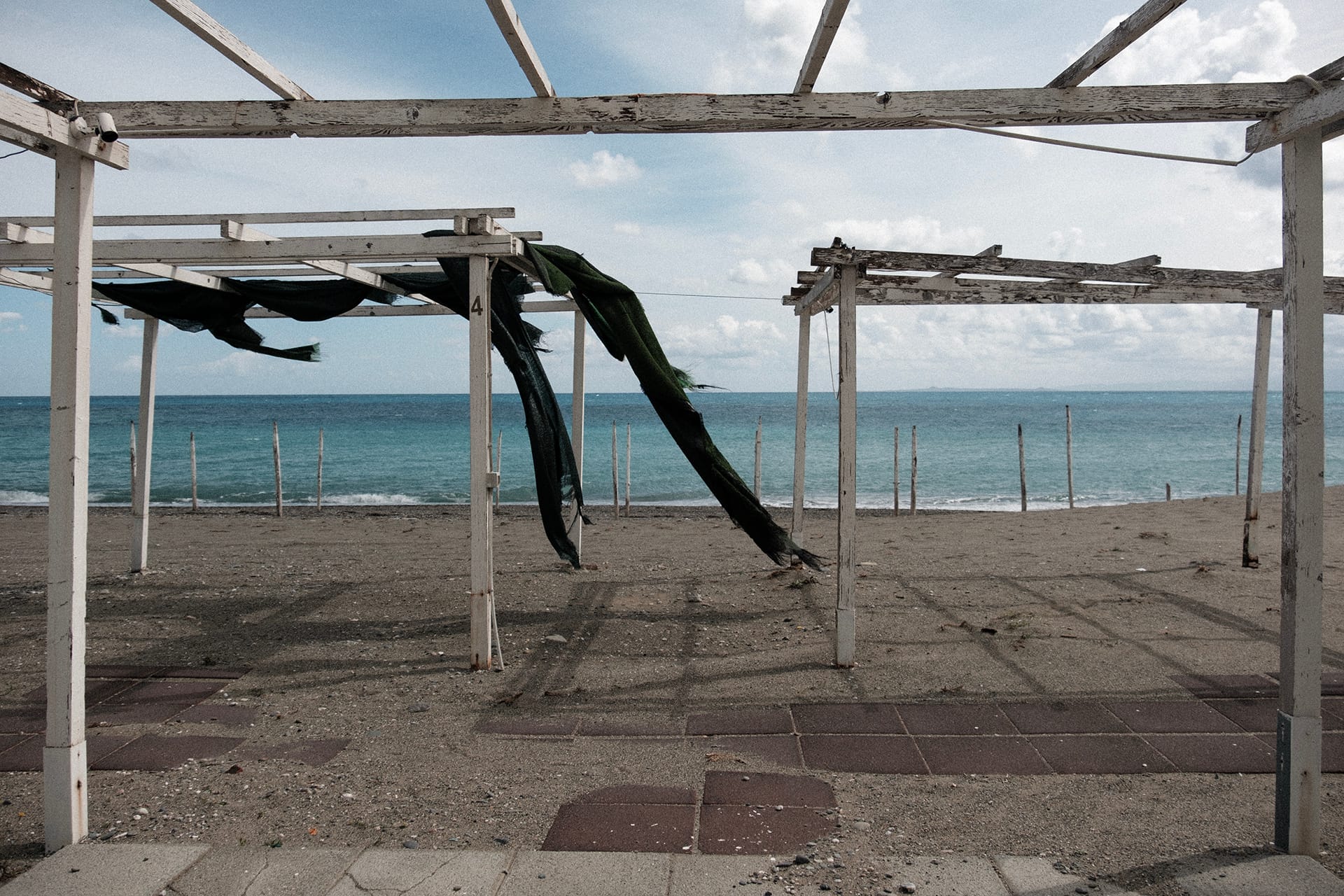 Un lido vuoto fuori stagione, con i teli strappati dal vento e il mare dietro
