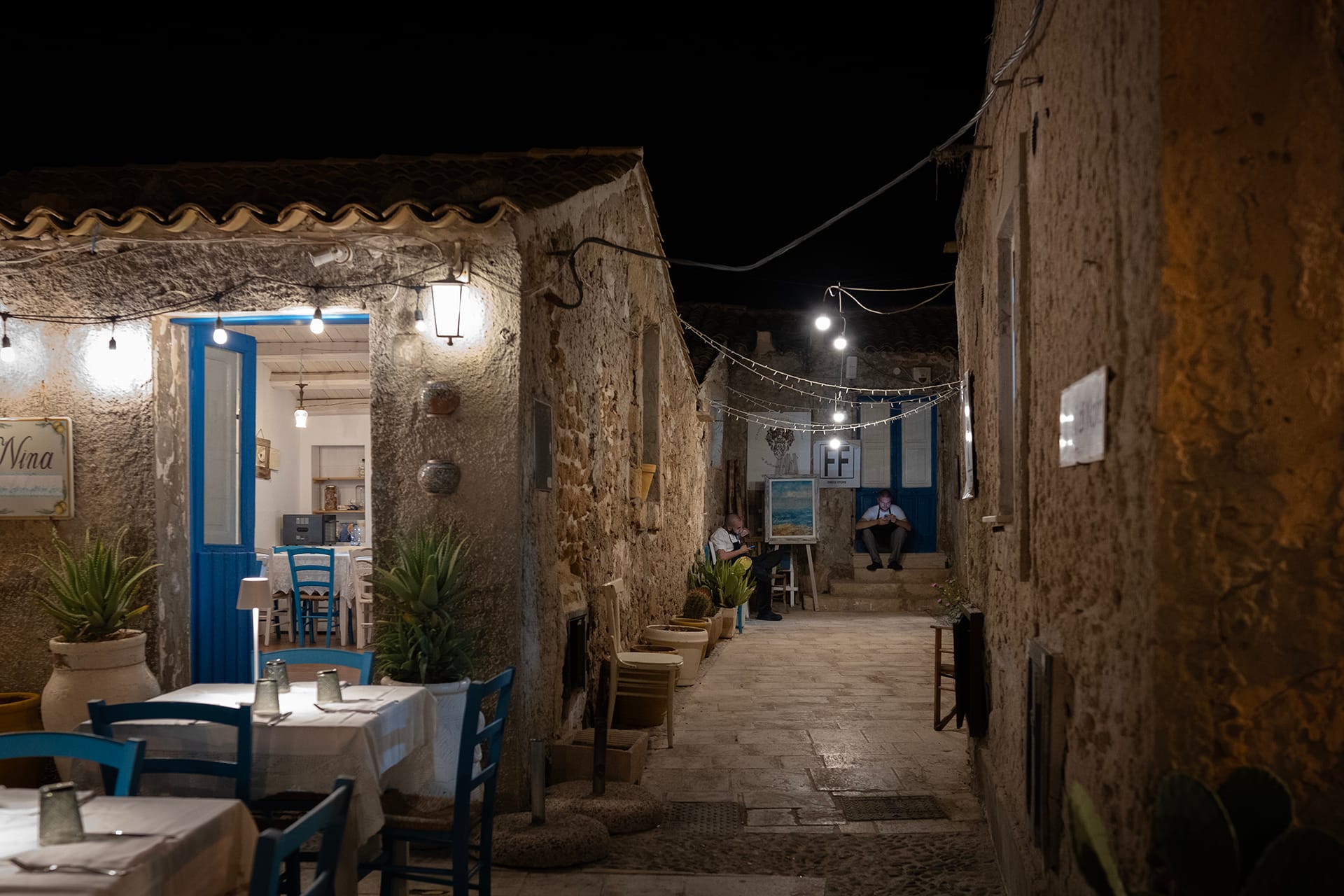 Vicolo di notte con tavolini all’aperto e luci calde tra i muri in pietra