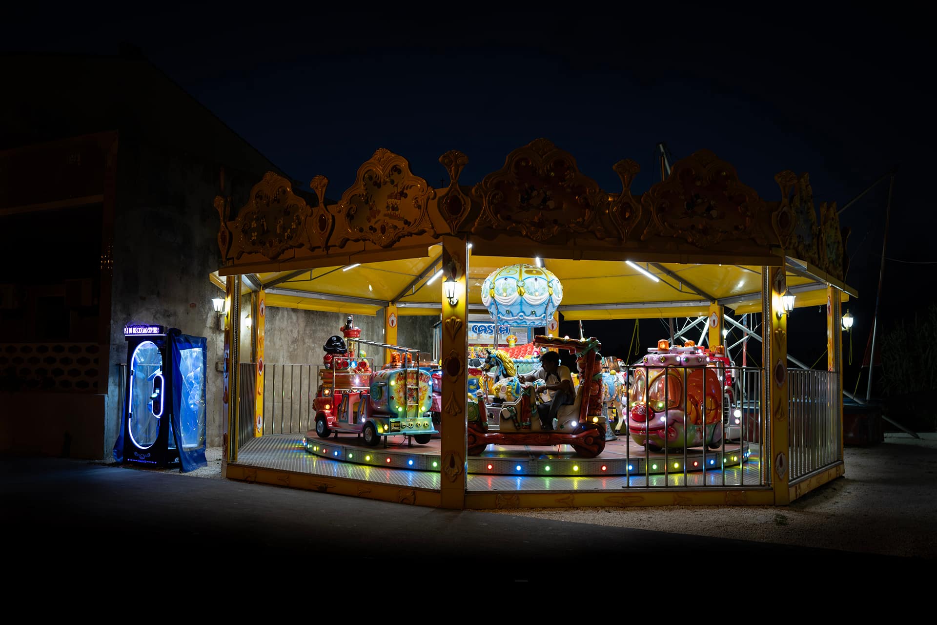 Giostra per bambini illuminata di notte, con luci colorate e un uomo seduto da solo al centro
