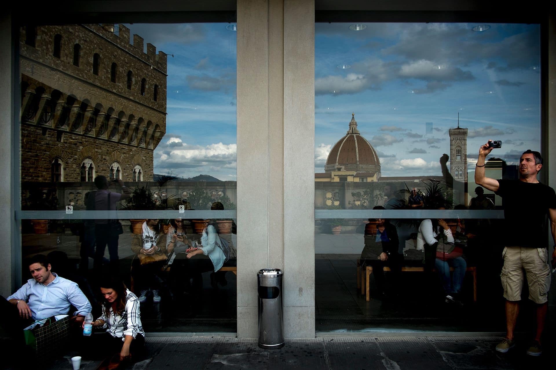 Riflesso in una vetrata di Firenze con la cupola del Duomo e Palazzo Vecchio, persone sedute sotto