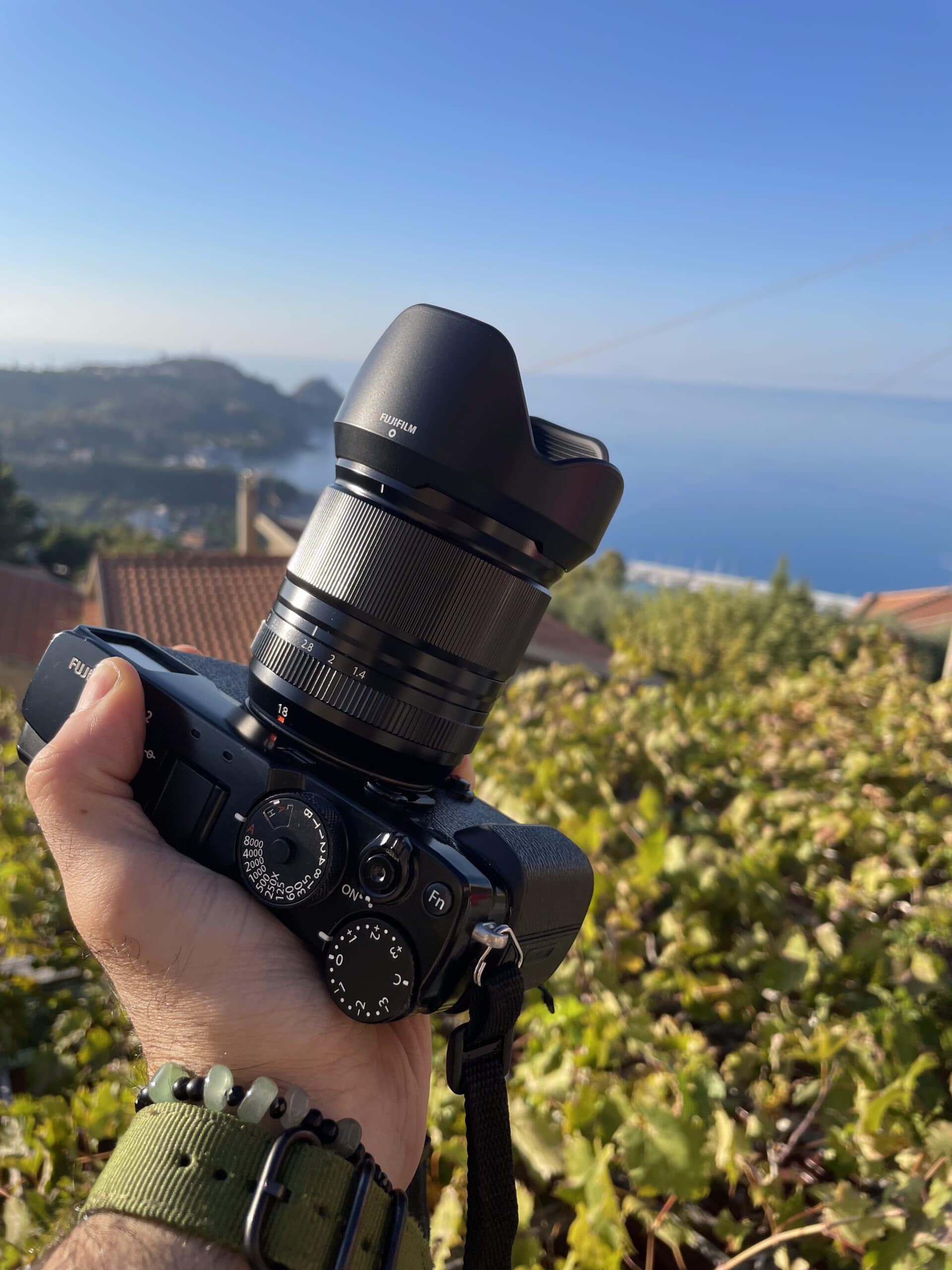 Fujifilm X-Pro2 con l’obiettivo Fujinon 18mm f/1.4 tenuta in mano, con il paesaggio di Erice sullo sfondo