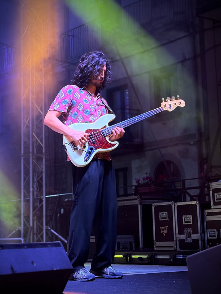 Bassista illuminato da un fascio di luce, con la facciata e i balconi della piazza dietro