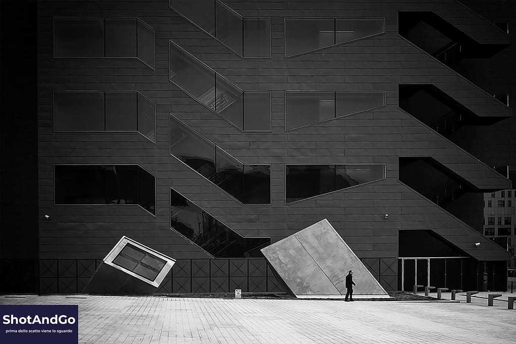 Figura umana davanti a un edificio dalle geometrie moderne in una fotografia in bianco e nero, esempio di allenamento dello sguardo fotografico.