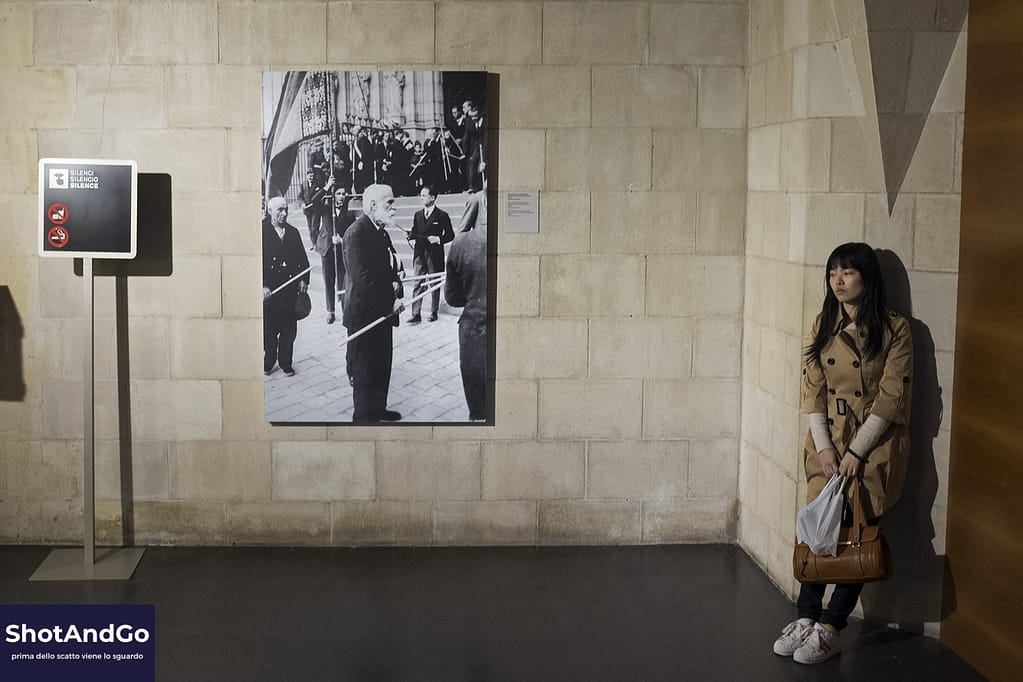 Fotografare non è collezionare immagini: è costruire uno sguardo Visitatrice osserva una fotografia in un museo, creando un dialogo tra immagine, spazio e osservazione.