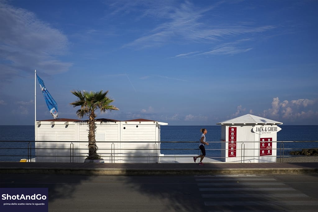 Lungomare con cabine, una palma e un corridore isolato nell’inquadratura, esempio di composizione essenziale e selezione degli elementi fotografici.