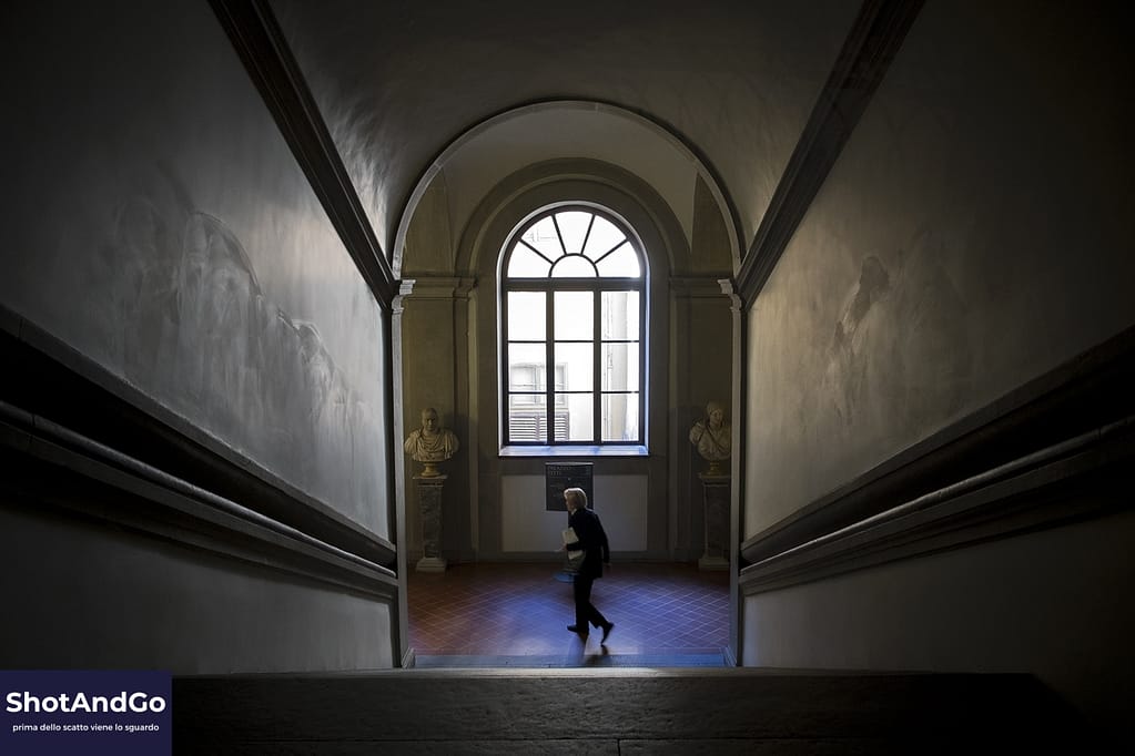 Guida 4 — La scelta: perché la scelta nella fotografia è più importante dello scatto Persona che attraversa il pianerottolo di una grande scala monumentale, incorniciata da linee architettoniche che guidano lo sguardo e rappresentano il concetto di scelta nella composizione fotografica.