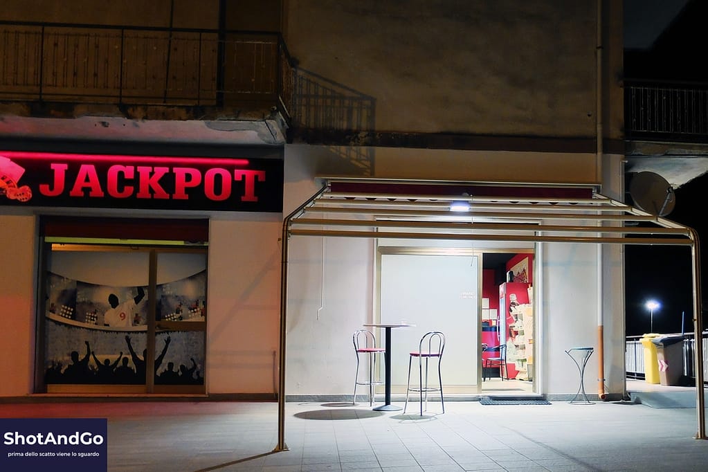 Guida 6 — Il perché: perché fotografare, davvero? Insegna luminosa “Jackpot” accanto a un locale illuminato durante la notte, fotografia urbana che richiama il tema della ricerca di significato oltre il risultato.