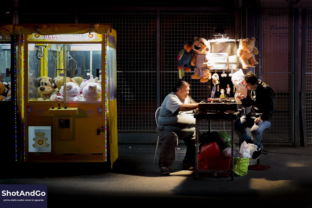 Due persone conversano accanto a una giostra in una strada pubblica di notte, esempio di street photography che pone questioni etiche e legali.