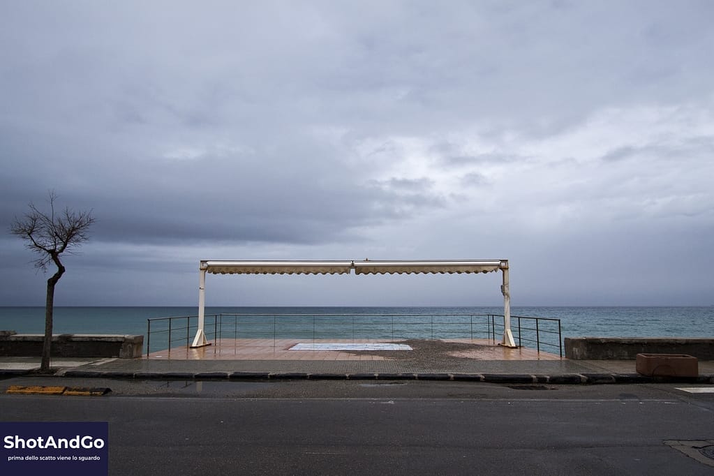 Struttura affacciata sul mare sotto un cielo nuvoloso, fotografia che invita a osservare oltre il soggetto.