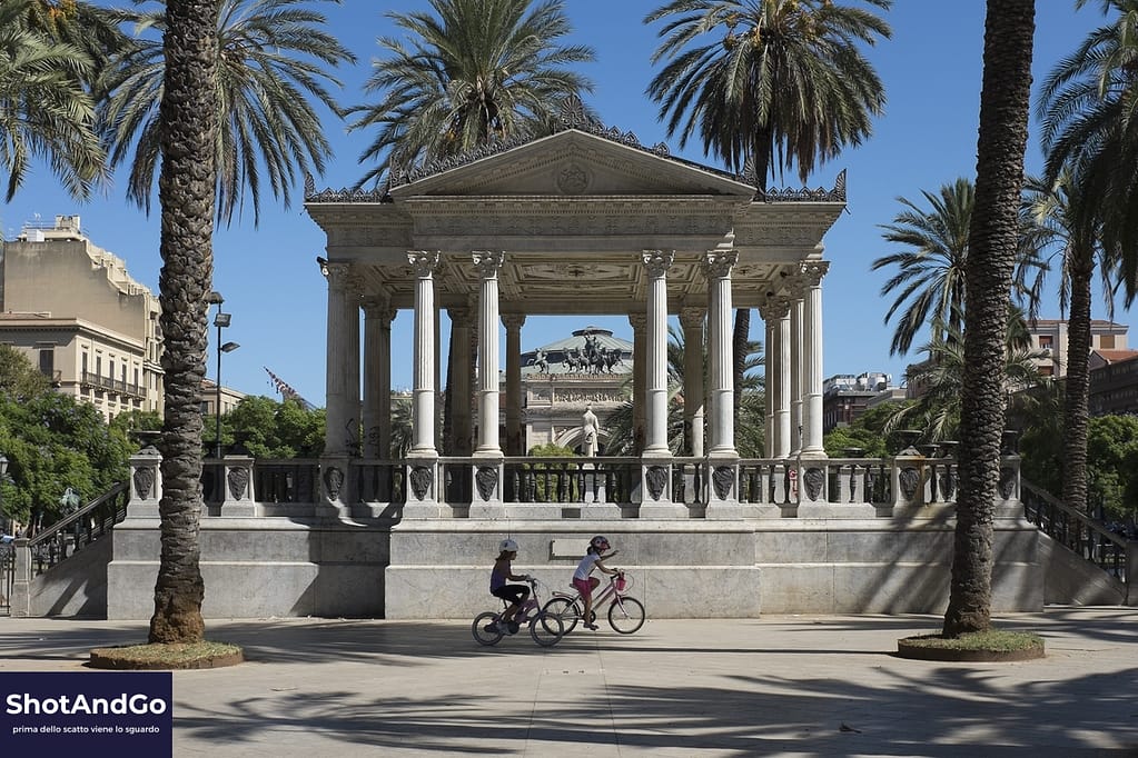 Tempietto monumentale con due ciclisti che attraversano la scena in una giornata di sole.