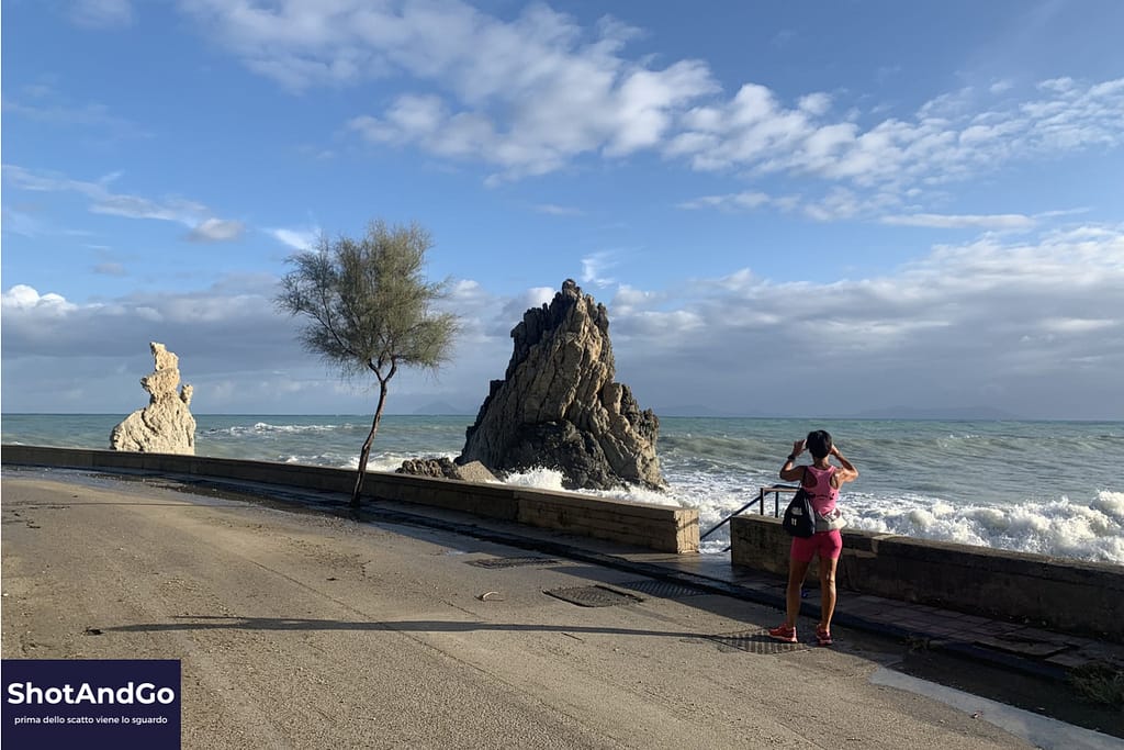 Persona che osserva e fotografa il mare davanti a una scogliera, esempio di attenzione e osservazione prima dello scatto fotografico.