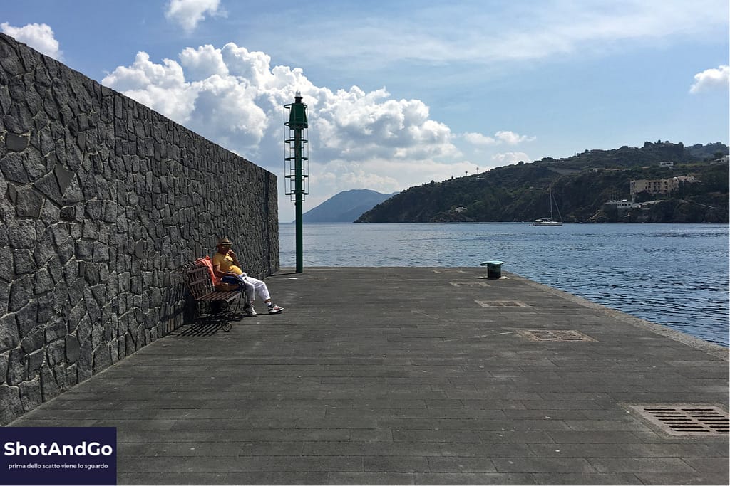 Fotografia con lo smartphone: come realizzare immagini che sembrano scattate con una fotocamera Persona seduta sul molo davanti al mare fotografata con uno smartphone, esempio di composizione e sguardo fotografico.